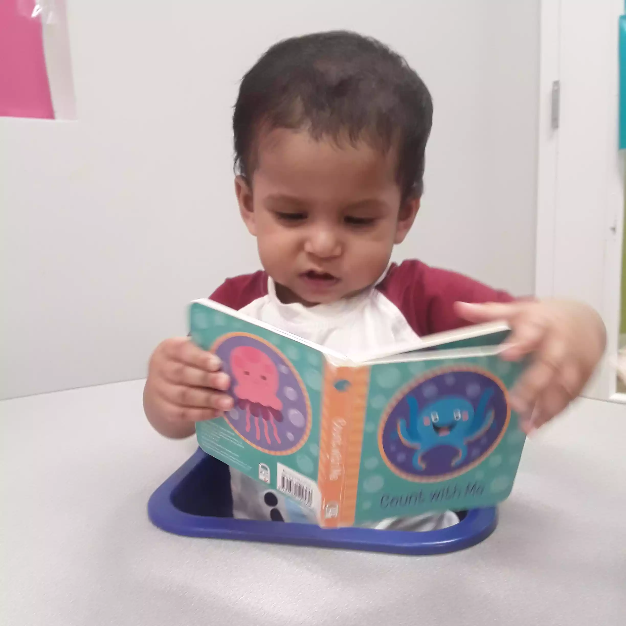 Infant Turning Pages of an Ocean Picture Book Infant reading board book at feeding table in daycare