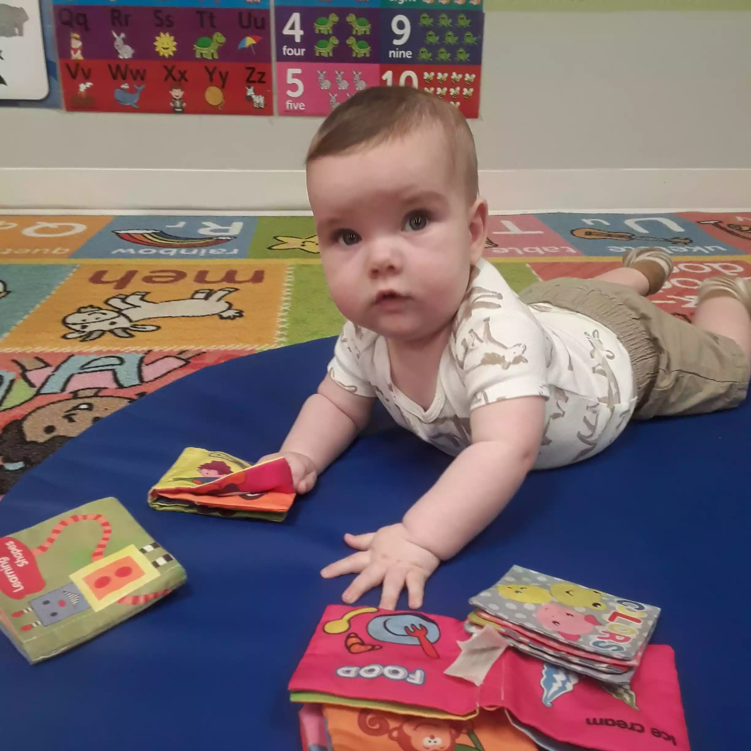 Infant Tummy Time Exploration with Soft Fabric Books Infant enjoying tummy time play on a mat with colorful soft books in classroom
