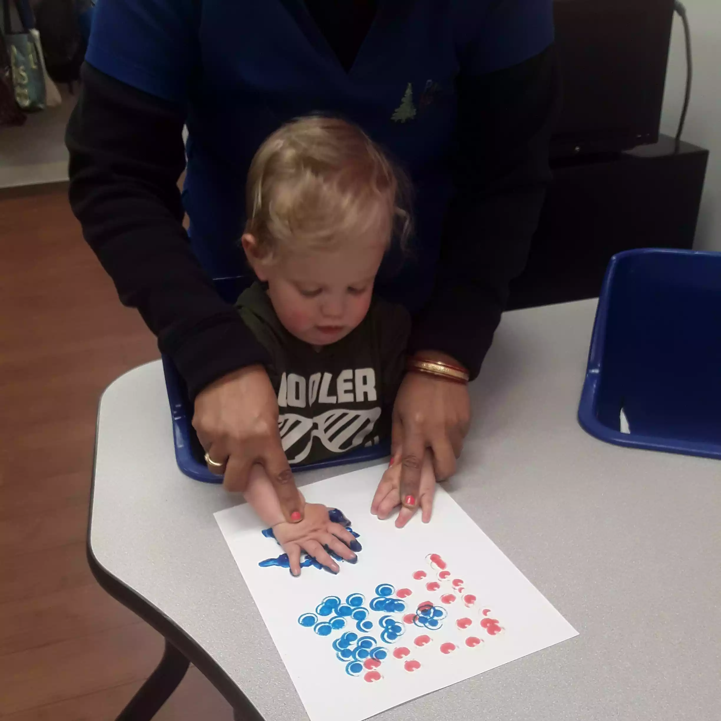 Infant Creating Handprint Painting with Teacher Assistance Teacher helping infant with handprint sensory art project during daycare program