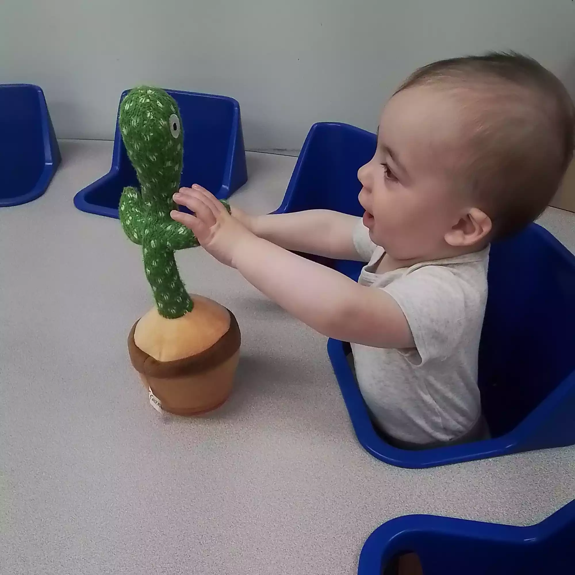 Infant reaching for dancing cactus sensory toy at activity table in daycare