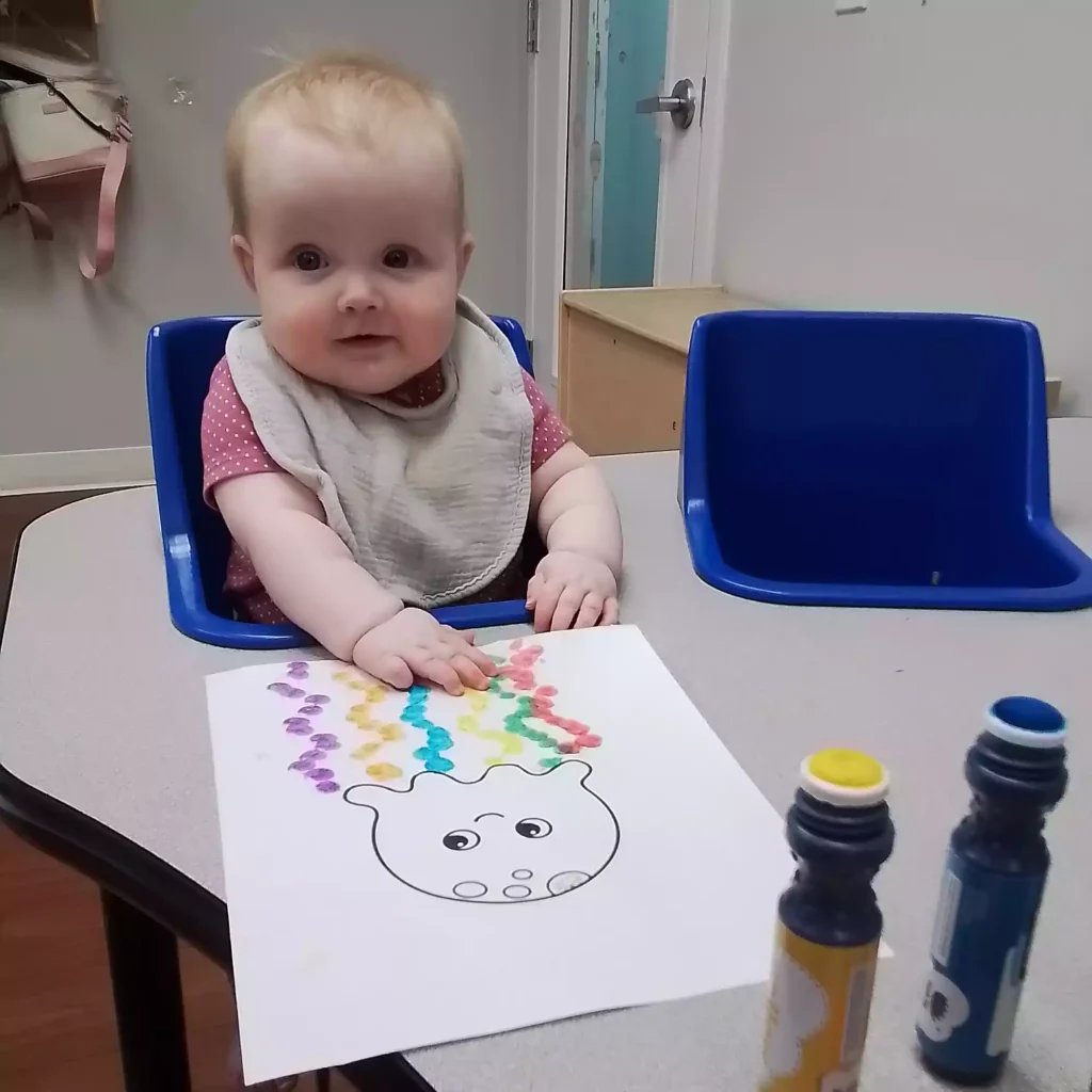Infant creating jellyfish dot marker artwork at activity table in classroom
