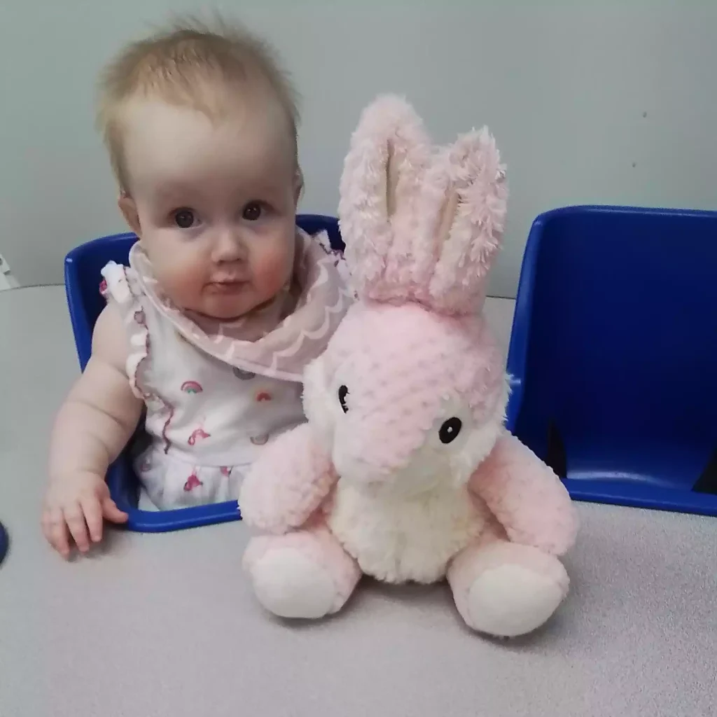 Infant seated with plush bunny toy during sensory play in daycare classroom