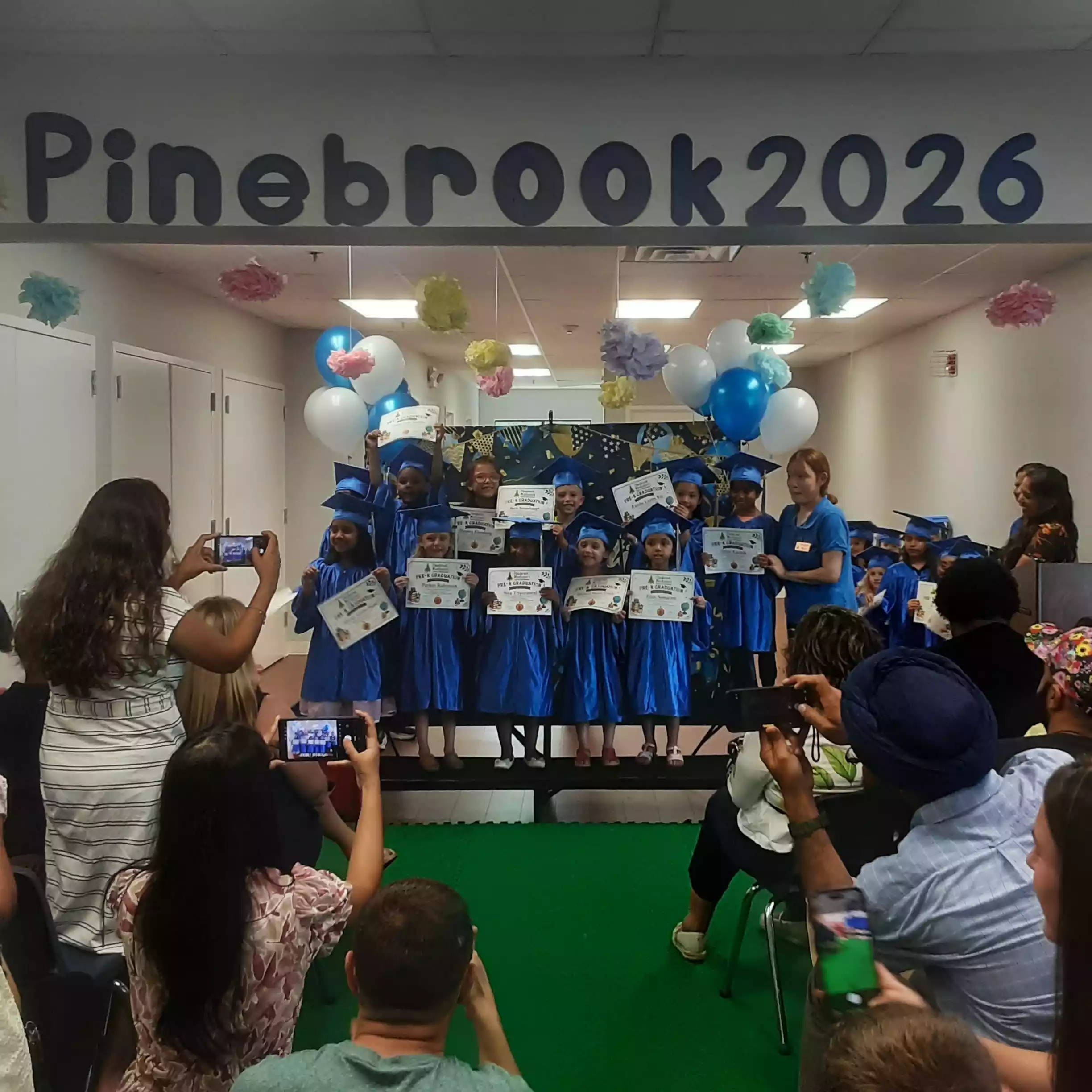 Pre-K graduates in blue caps and gowns holding diplomas on stage