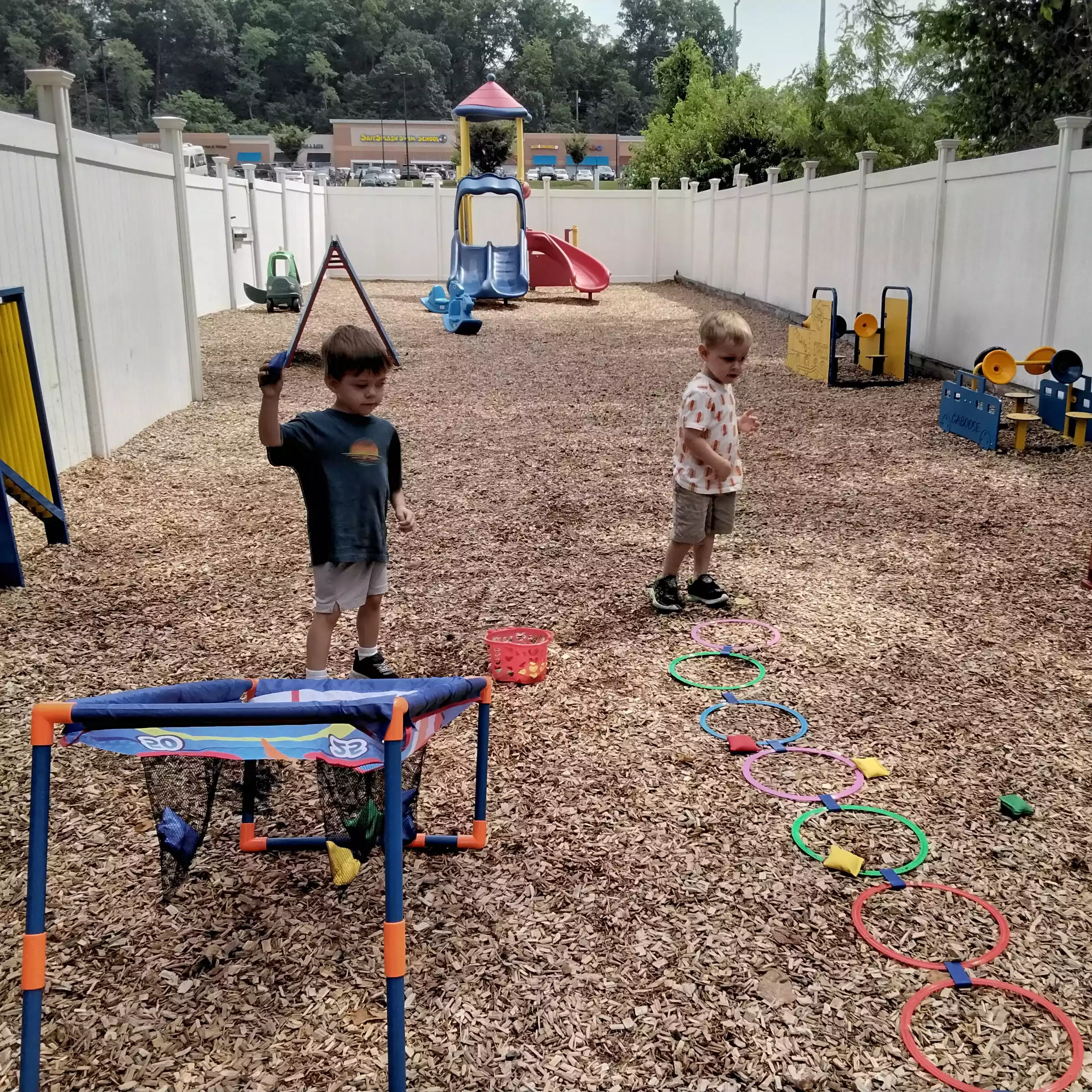 Pinebrook Pre-K Students Playing Playground Beanbag Game Two boys taking turns throwing beanbags at a target on a woodchip playground.