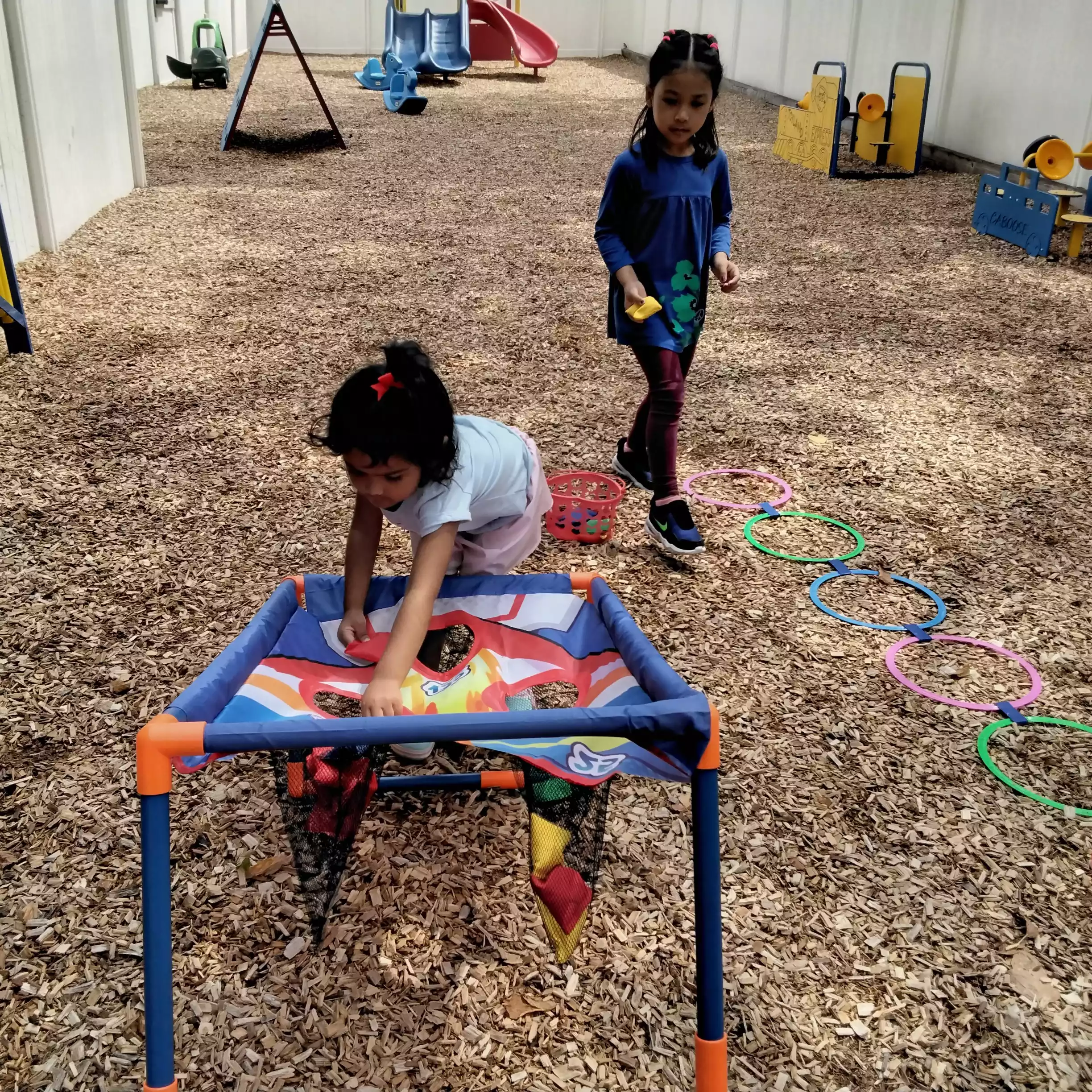 Pinebrook Pre-K Student Reaching into Target Net A young girl reaching into a net target during an outdoor lawn game while another girl walks nearby.